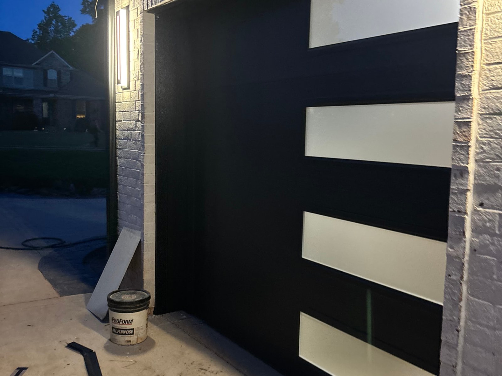 Freshly painted matte black garage door with frosted glass panels and painted brick trim